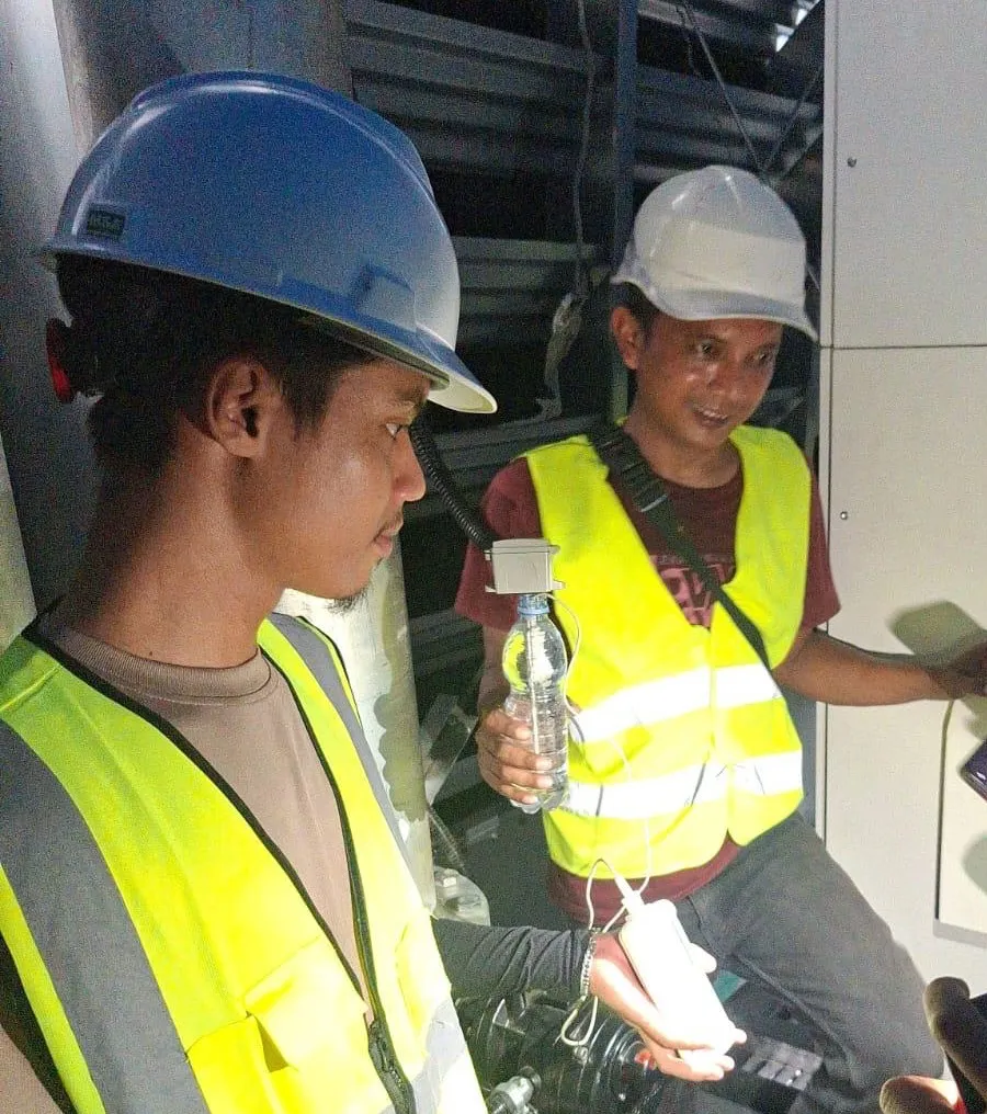 Teknisi Pariksa berhelm biru memperhatikan engineer memeriksa pembacaan sensor di proyek data center.