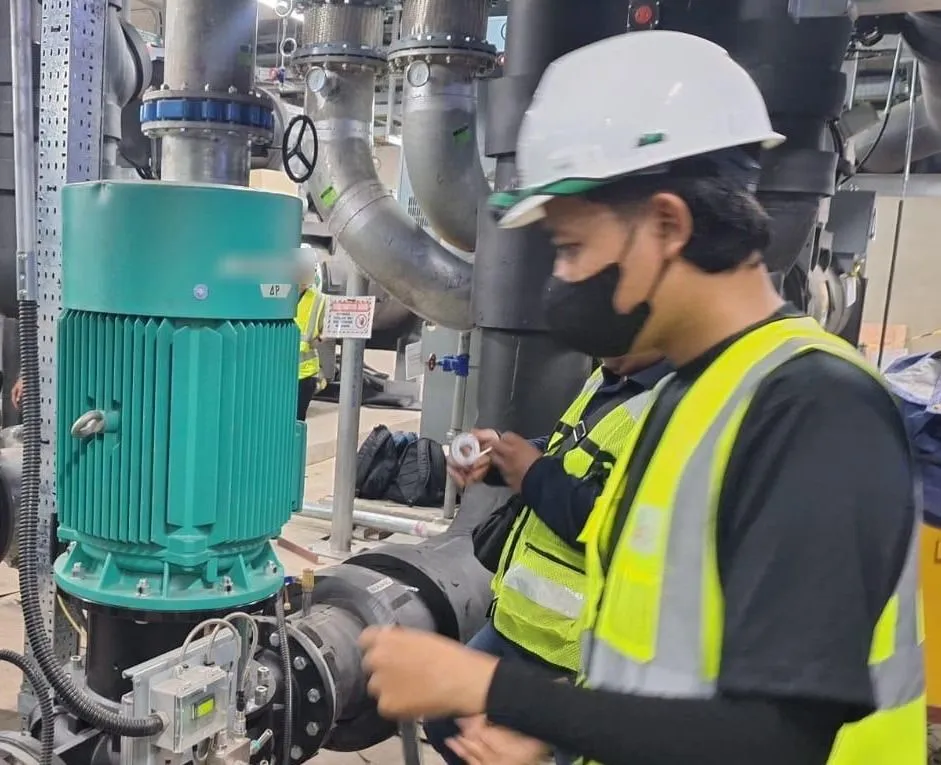 A Pariksa engineer preparing instruments beside the chilled water pumps in a plant room.